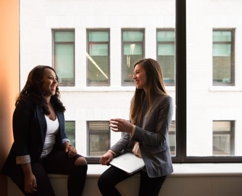 2 professional women chatting on an office window sill