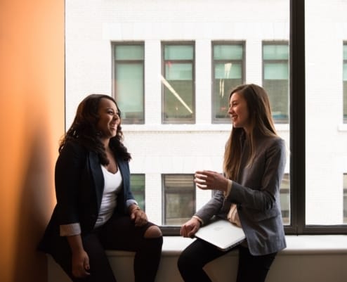 2 professional women chatting on an office window sill